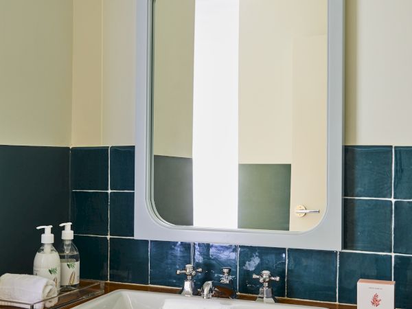 A small bathroom sink with a white basin, blue tile backsplash, a rectangular mirror, and a wooden counter. The top light fixture sits above the mirror.