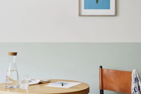 A minimalist room with a round wooden table, water carafe, papers, leather chair, and framed wall art depicting a swimming pool.