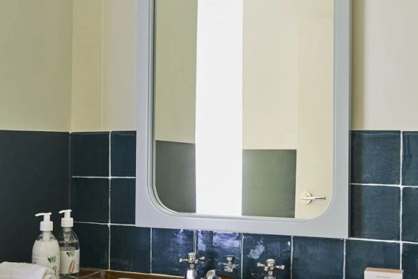 A bathroom sink with soap dispensers, a towel, and a mirror above it, surrounded by dark blue tiles.