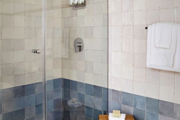 A bathroom with a glass-enclosed shower, tiled walls, a towel on a rack, and a wooden bench with a towel and soap.