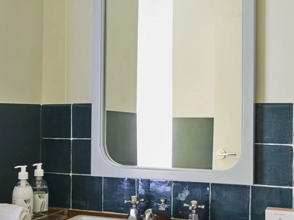 A bathroom with a mirror, sink, two soap dispensers, hand towel, and dark blue tiles on the wall.