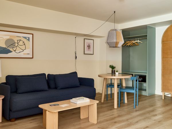 A cozy living area with a navy sofa, light wood coffee table, wall art, and a small round dining set with blue chairs in an open-plan space.