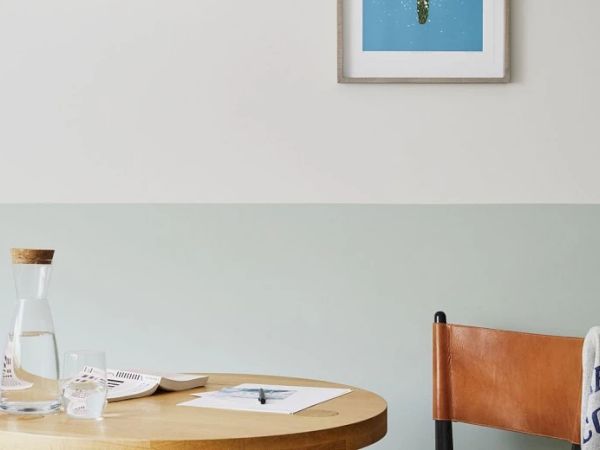 A wooden table with a glass water pitcher, papers, and books, next to a leather chair, under a framed picture of a cactus on the wall.
