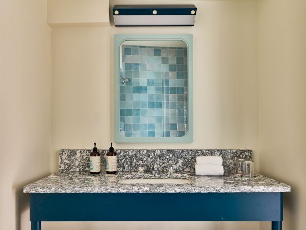 A small bathroom vanity with a blue frame, speckled granite counter, two bottles, a folded towel, and a mosaic tile mirror above.