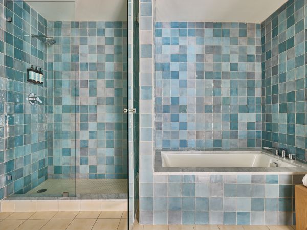 A modern bathroom with blue mosaic tiles, a glass shower, and a built-in bathtub; towels on a wood vanity to the right.
