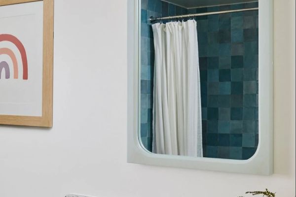 This image shows a bathroom with a mirror reflecting a shower curtain and blue tiles, a framed picture on the wall, and part of a countertop.