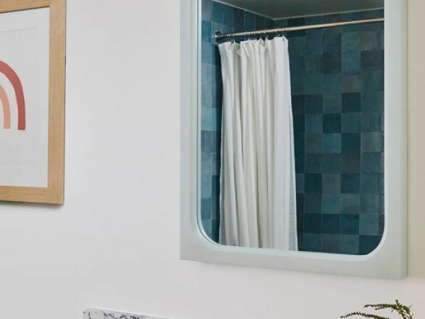The image shows a bathroom mirror reflecting a shower with teal tiles and a white curtain, next to a picture of a rainbow on the wall, ending the sentence.