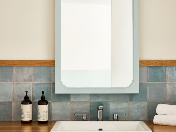 A clean, modern bathroom sink setup with a rectangular mirror, blue-tinted frame, frosted glass doors, and neatly stacked towels above a wooden counter.
