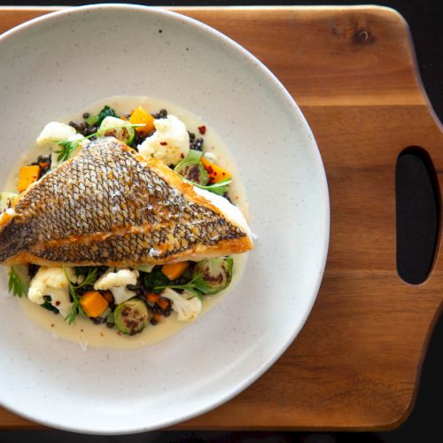 A plated dish featuring a crispy-skinned fish fillet atop a creamy vegetable medley on a white plate, arranged on a wooden tray.