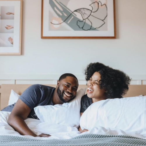 A couple cuddles on a bed, smiling at a notebook together, cozy and intimate moment.