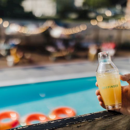 A sunny poolside scene with a bright blue pool, a person in a yellow shirt standing near the edge, and a relaxing, vacation vibe.