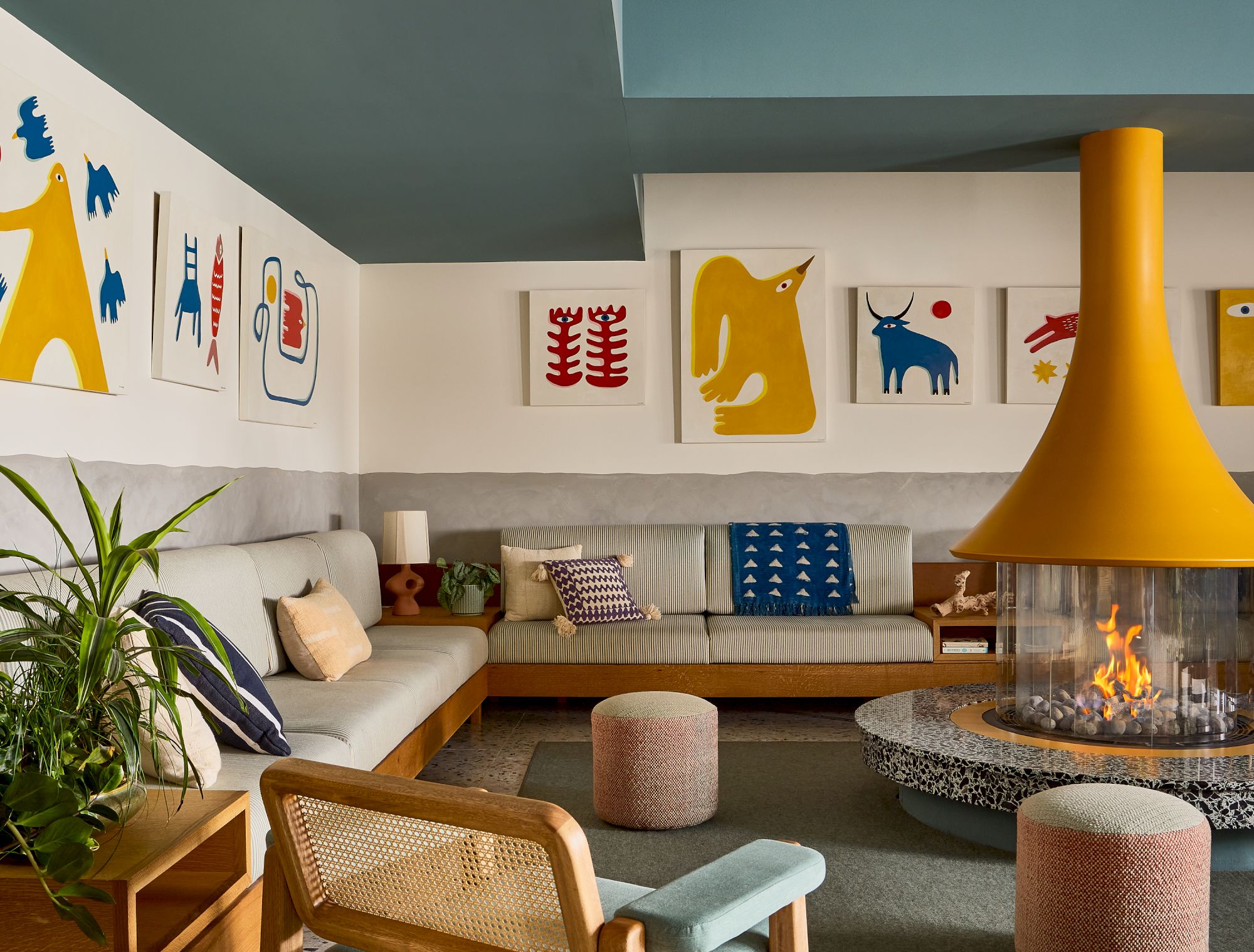 Cozy modern living room with a circular fireplace, airy seating, bright animal-themed wall art, and green plants for a playful vibe.