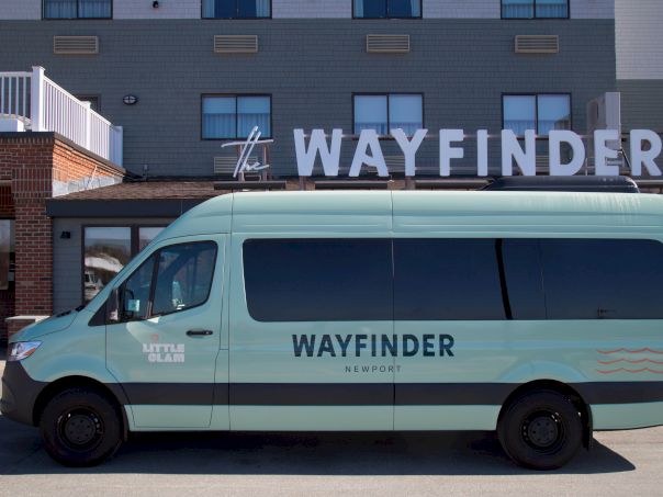 A light blue Wayfinder Renault van parked in front of a building with large &ldquo;WAYFINDER&rdquo; letters on the facade, under a clear sky.