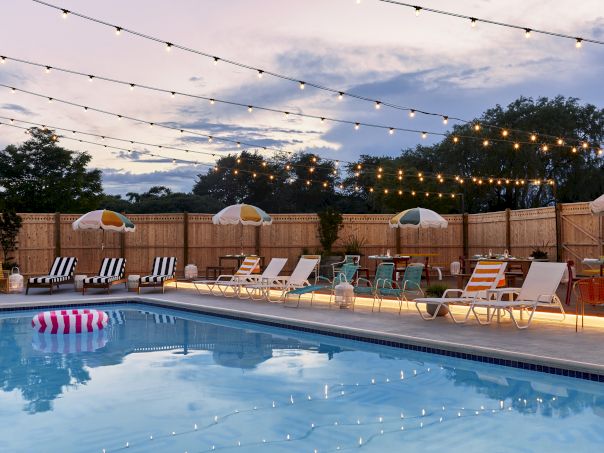 A nighttime pool area with string lights, lounge chairs, umbrellas, and a calm blue pool reflecting the lights.