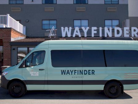 A light blue Wayfinder van is parked in front of a building with large &ldquo;WAYFINDER&rdquo; lettering on the sign.