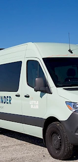 A mint-green Mercedes van labeled &ldquo;WAVWRIDER&rdquo; parked on a gravel lot with a clear blue sky behind it.