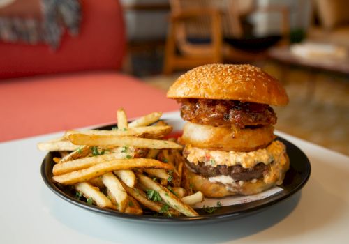 A plated cheeseburger with onion rings or fries on the side, served on a black plate with a crispy bun, and a casual dining setting.