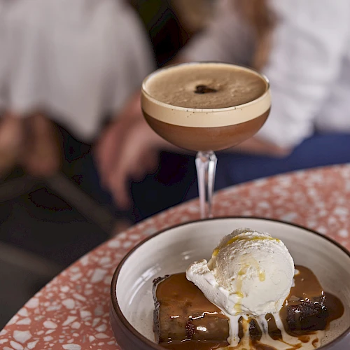 A fancy dessert: a caramel sauce cake with a scoop of vanilla ice cream, drizzled with caramel, in a small bowl, and a cocktail glass above it.