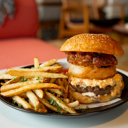 A plated cheeseburger with onion rings or fries on the side, served on a black plate with a crispy bun, and a casual dining setting.