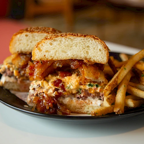 A cheesy stacked sandwich with melted cheese and bacon, served with crispy French fries on a black plate.