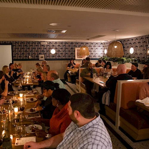 A crowded restaurant with people dining at booths and tables, warm lighting, and a cozy, busy atmosphere.