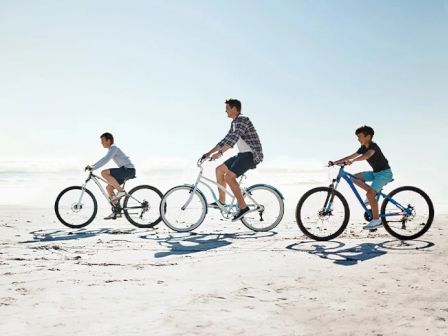 Three people are riding bicycles on a sunny beach.