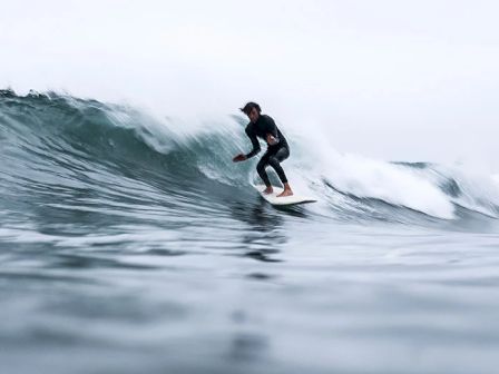 A surfer rides a breaking wave on a surfboard in the ocean, wearing a wetsuit.