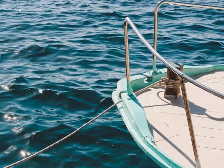 A boat's deck with a railing and a rope tied to it is shown, with the surrounding blue water.