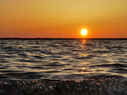 A vibrant sunset over a calm ocean, with the sun's reflection shimmering on the water's surface, creating a serene and peaceful atmosphere.