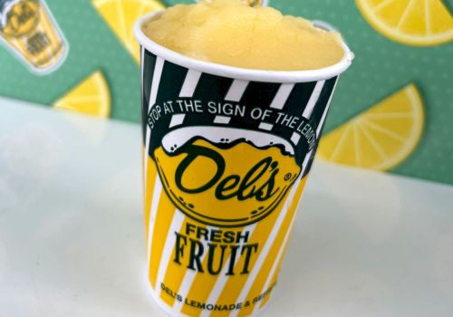 A striped lemon cup with yellow fruit slush, bold &ldquo;Deli&rsquo;s&rdquo; logo, and fresh fruit graphics in the background, topped with a foamy scoop.