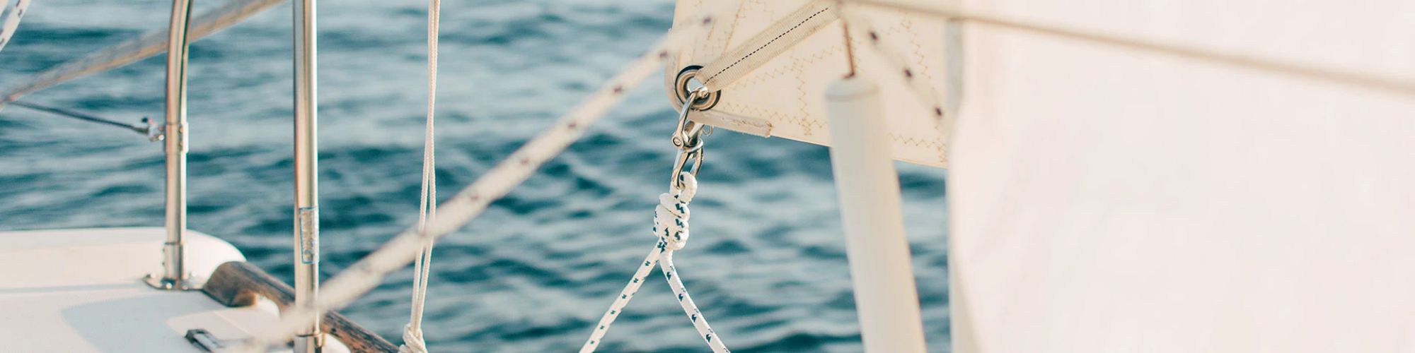 The image shows a close-up of a sailboat's deck and rigging with the ocean visible in the background.