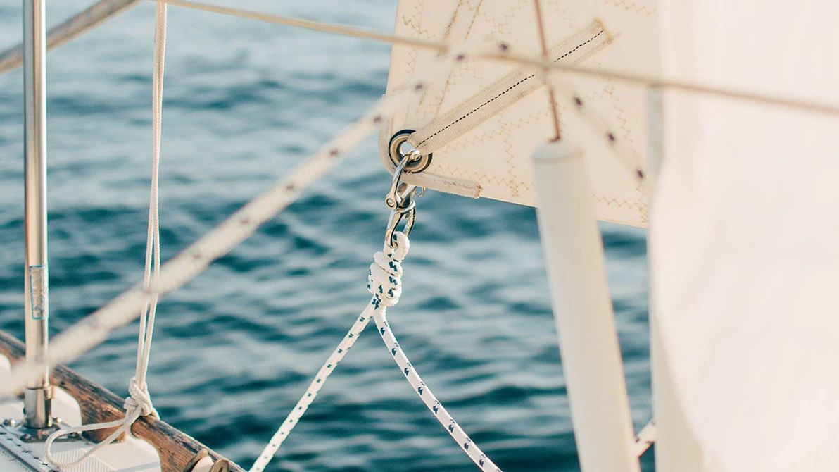 The image shows a close-up of a sailboat's deck and rigging with the ocean visible in the background.