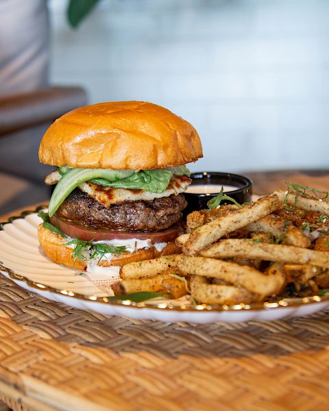 A juicy hamburger with lettuce and onions accompanied by seasoned fries on a wicker plate.