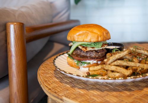 A juicy hamburger with lettuce and onions accompanied by seasoned fries on a wicker plate.