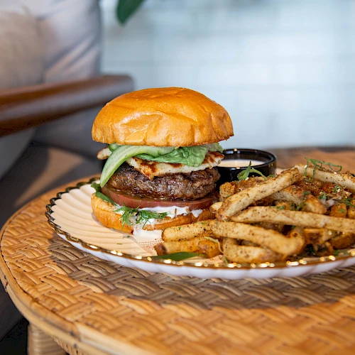 A juicy hamburger with lettuce and onions accompanied by seasoned fries on a wicker plate.