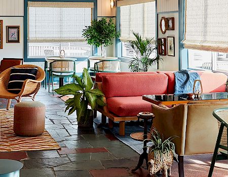 This image shows a cozy, stylish lounge area with modern furniture, potted plants, and large windows letting in natural light.