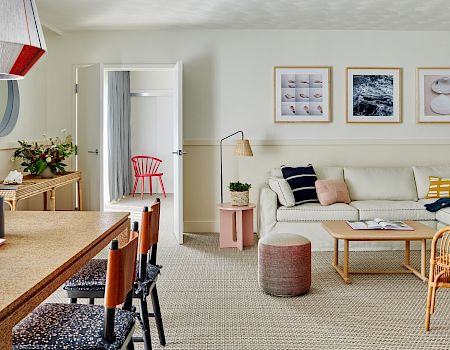 A cozy living room with a sofa, coffee table, colorful art, dining table with chairs, and a stylish light fixture.