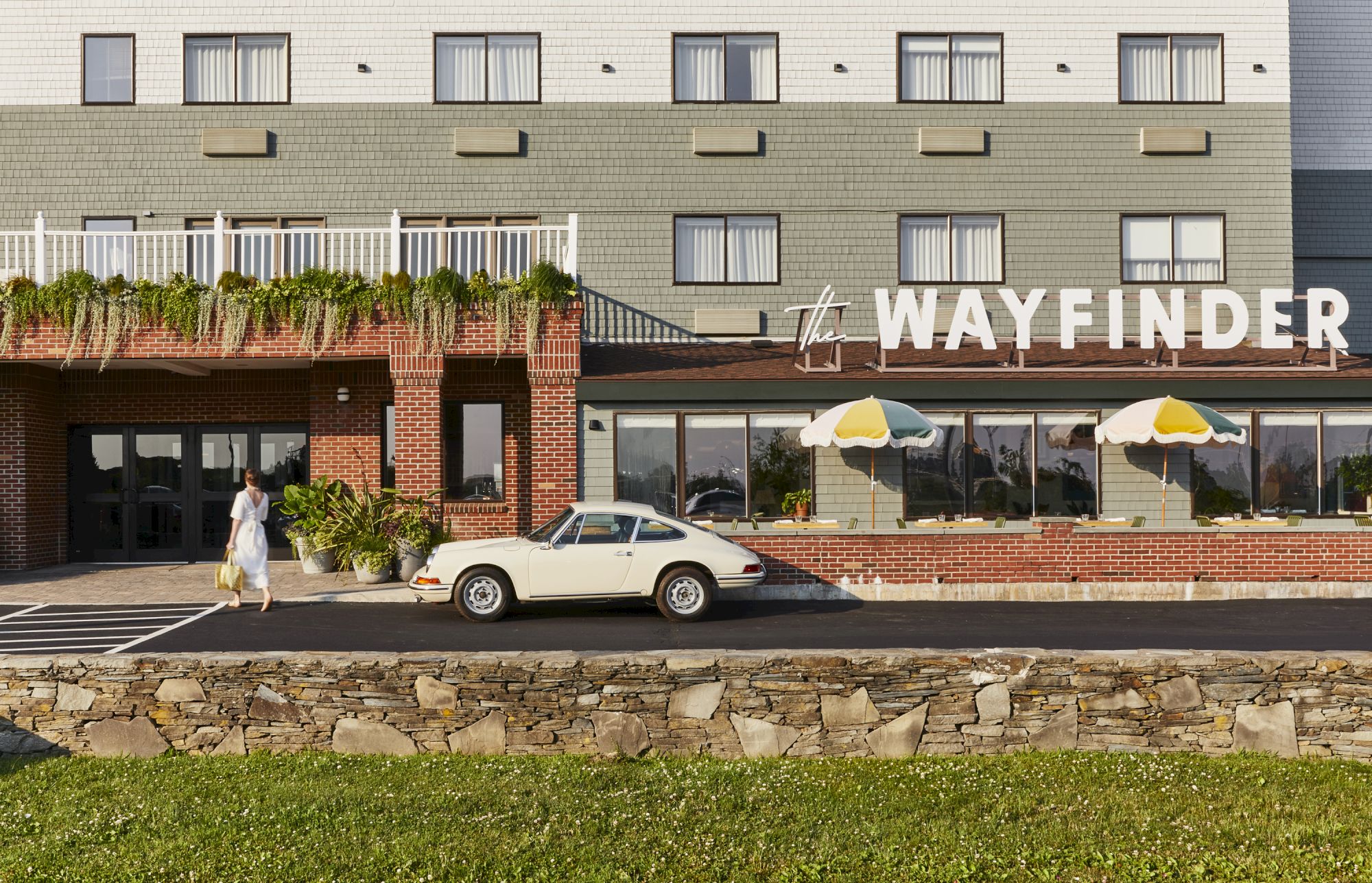 A HOTEL or motel named Wayfinder with a vintage car parked in front and two yellow umbrellas by the entrance.