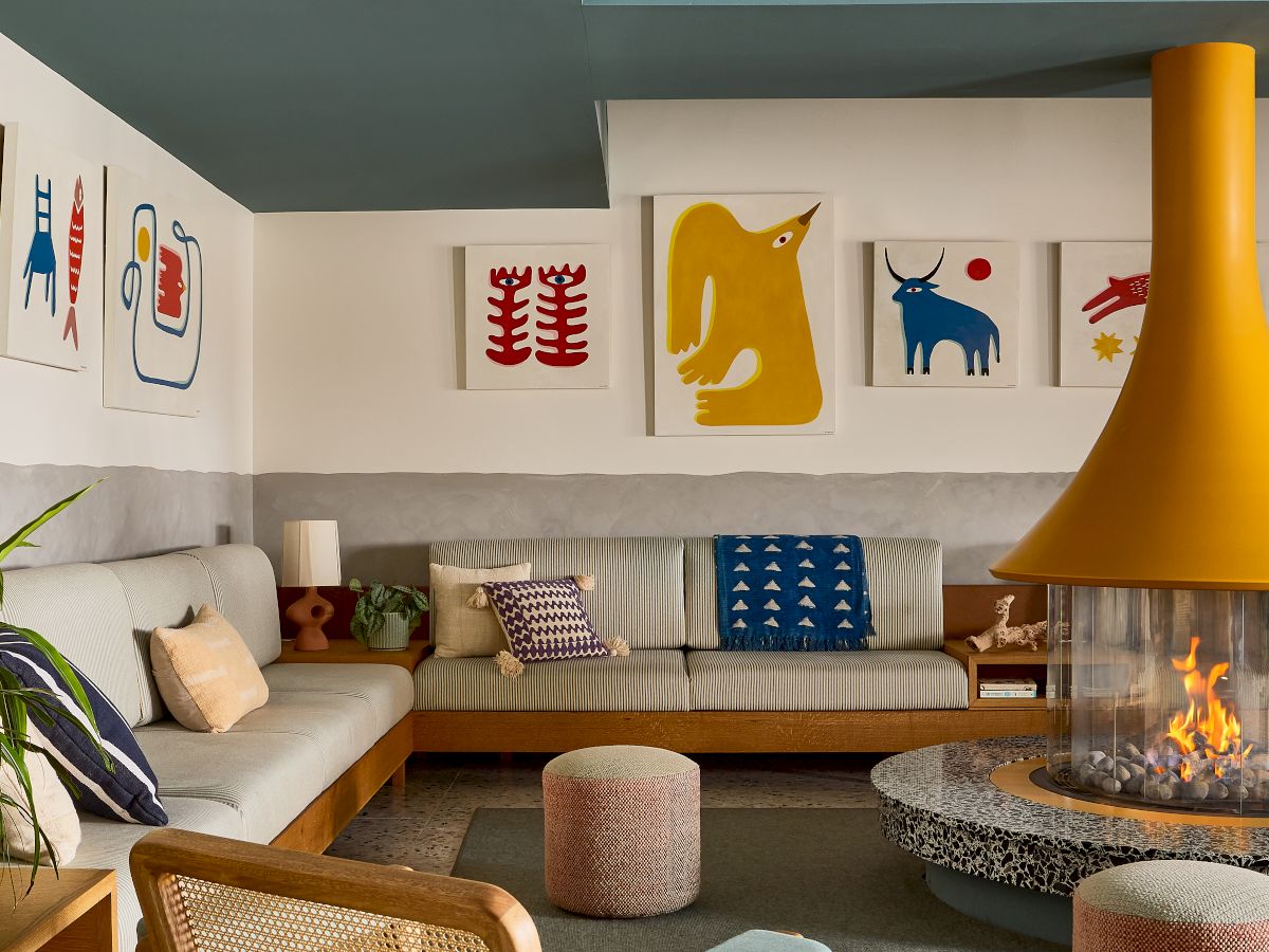 Cozy living room with light wood furniture, pale blue walls, a bright orange fireplace hood, abstract animal artwork, and a cream sofa with patterned cushions.