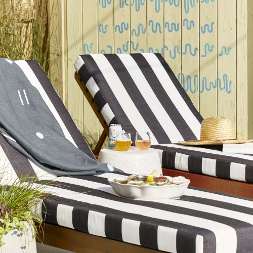 Outdoor scene with striped lounge chairs on a wooden deck, a weathered chalkboard sign, and a sunny, relaxed vibe.