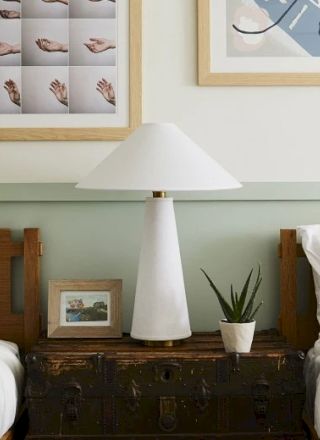 A cozy bedroom with two single beds, a shared nightstand with a lamp, framed pictures on the wall, and a small potted plant.