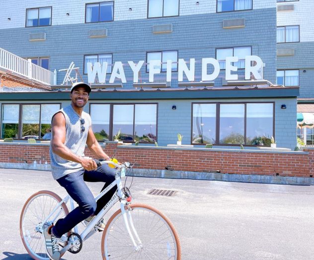 A person is riding a bicycle in front of a building with a sign that reads 