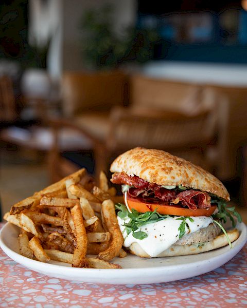 A cheeseburger with bacon, tomatoes, and greens beside a pile of fries on a plate at a restaurant table.