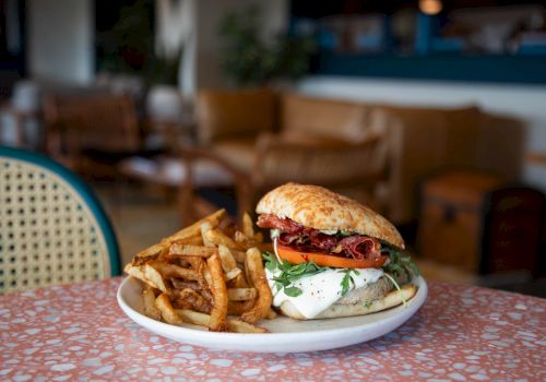 A cheeseburger with bacon, tomatoes, and greens beside a pile of fries on a plate at a restaurant table.