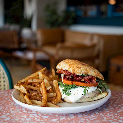 A cheeseburger with bacon, tomatoes, and greens beside a pile of fries on a plate at a restaurant table.