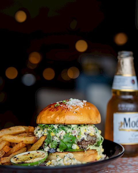 A cheeseburger with fries and a beer bottle on a plate, lit with warm bokeh lights in the background.