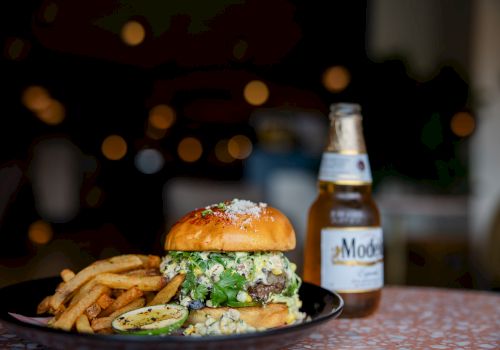 A cheeseburger with fries and a beer bottle on a plate, lit with warm bokeh lights in the background.