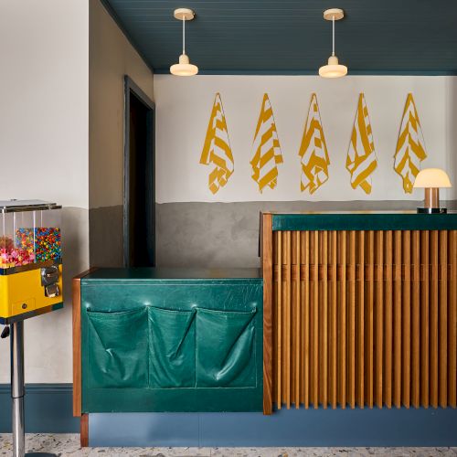 Indoor bar with a green counter, wood slats, pendant lights, yellow flag wall art, and a candy dispenser on the left.