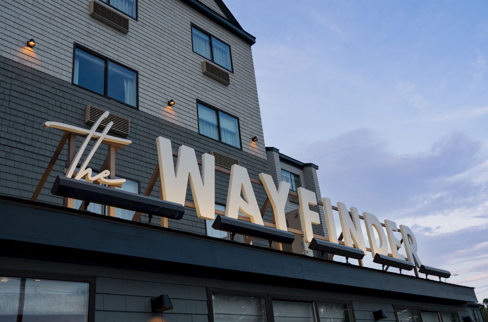 A hotel building facade with a large lit &ldquo;WELCOME CENTER&rdquo; sign, windows, and brick exterior under a dusk-blue sky.