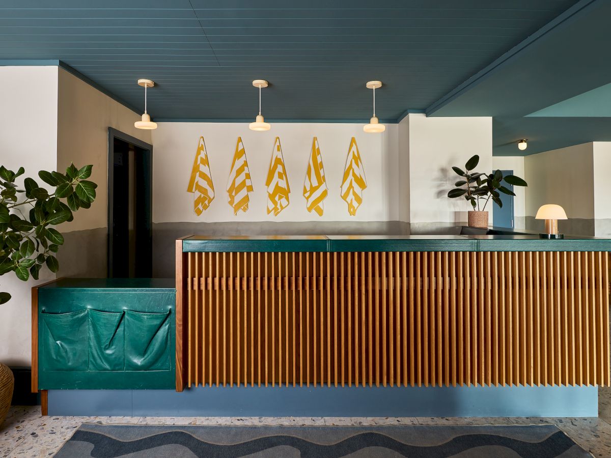 A modern reception counter with teal trim, pendant lights, wall flags, and potted plants in a clean lobby.